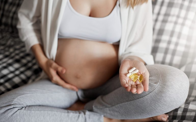Close up of young mother holding pills. Staying home to fight nausea and keep her birth healthy.