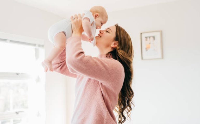 Proud young mother holding up baby close to face and smiling in living room