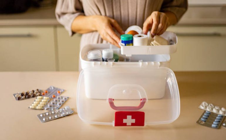 Closeup female hand neatly placing medicament at domestic first aid kit top view. Storage organization in transparent plastic box drug, pill, syringe, bandage. Fast health help safety emergency supply