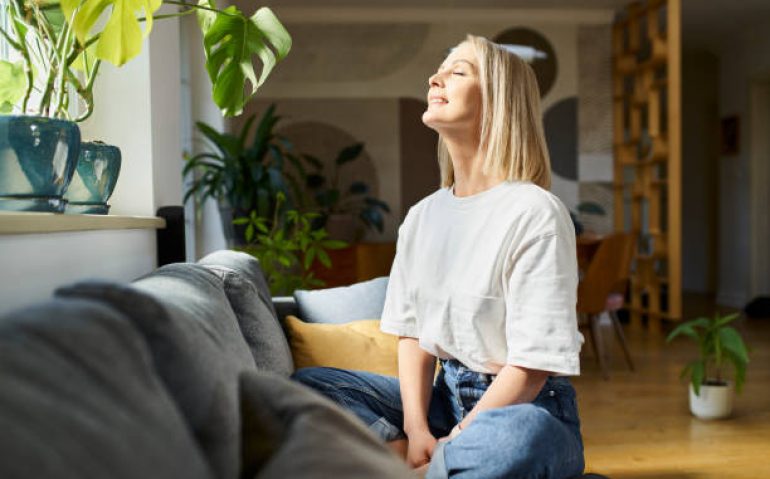 Happy adult woman sitting on the sofa with eyes closed enjoying bright daylight