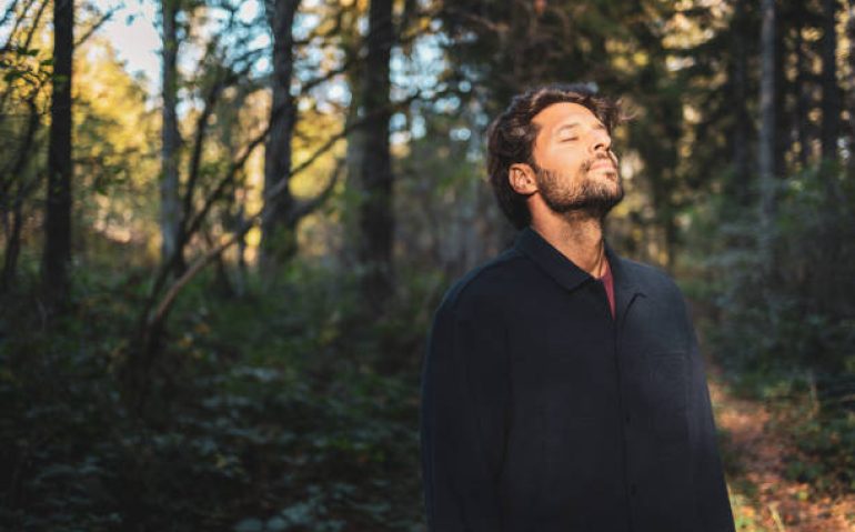 Man standing in the forest with his eyes closed enjoying the sun
